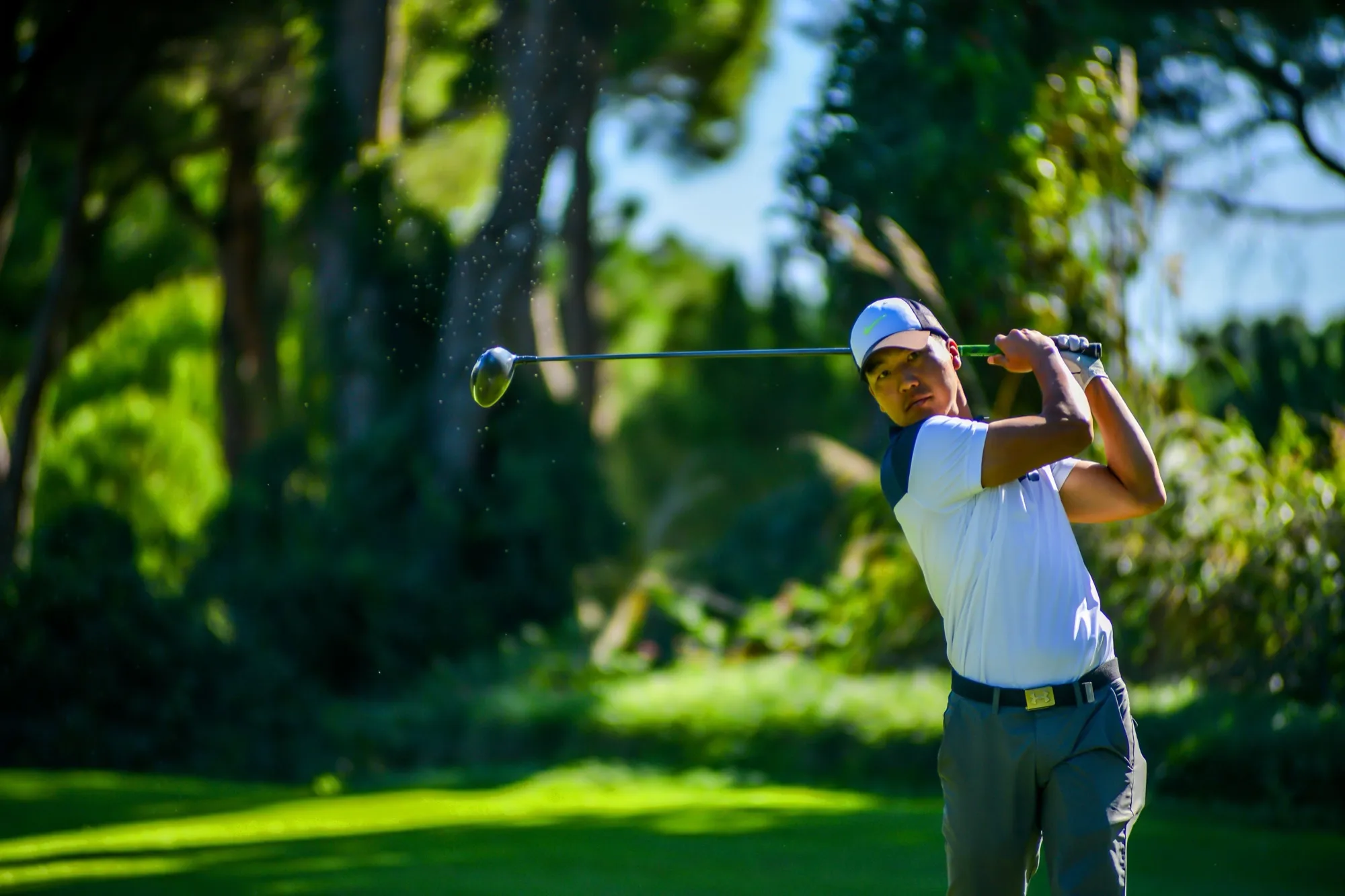 A golfer at the top of the follow-through on a tree-lined fairway